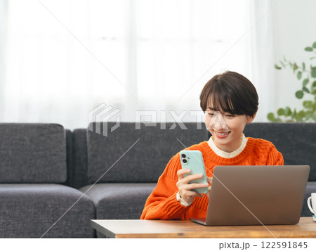リビングルームでノートパソコンとスマホを使う女性 リビングルームでノートパソコンとスマホを使う女性 122591845