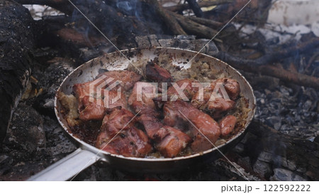 Sizzling, juicy meat is cooking over a roaring open flame in a large frying pan Sizzling, juicy meat is cooking over a roaring open flame in a large frying pan 122592222