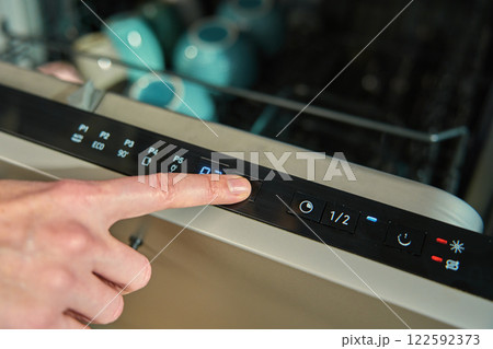 Finger pressing button on dishwasher control panel 122592373