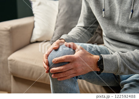 Man holding knee in pain while sitting on couch 122592488