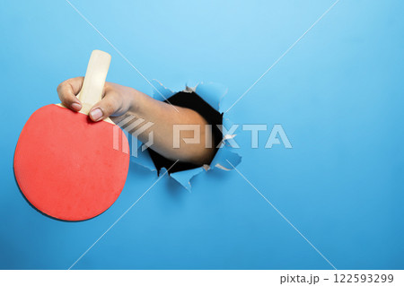 Human hand holding table tennis paddle through ripped paper. Mockup or Copy space. Concept of sport Human hand holding table tennis paddle through ripped paper. Mockup or Copy space. Concept of sport 122593299