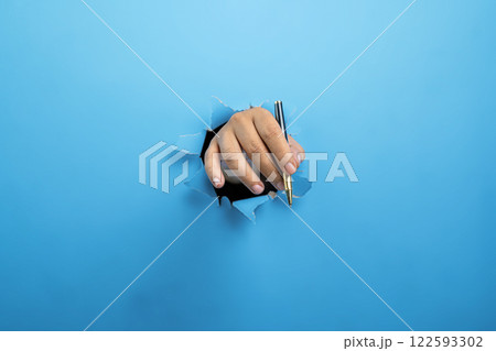Human hand holding ballpoint pen through ripped paper. Mockup or Copy space. Concept of business, signature, communication, or handwriting Human hand holding ballpoint pen through ripped paper. Mockup or Copy space. Concept of business, signature, communication, or handwriting 122593302
