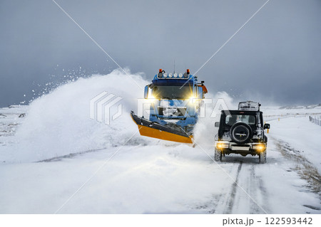 Car driving through a snow plow truck clearing snow from the road after the blizzard. Road and highway maintenance during winter Car driving through a snow plow truck clearing snow from the road after the blizzard. Road and highway maintenance during winter 122593442