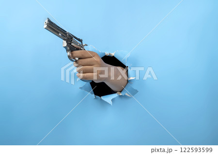 Human hand holding handgun through ripped paper. Hand gestures. Mockup or Copy space. Aiming weapons, war, crime, or violence Human hand holding handgun through ripped paper. Hand gestures. Mockup or Copy space. Aiming weapons, war, crime, or violence 122593599