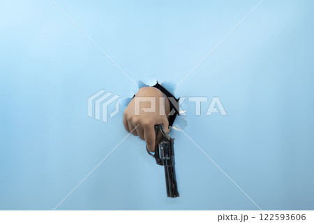 Human hand holding handgun through ripped paper. Hand gestures. Mockup or Copy space. Aiming weapons, war, crime, or violence 122593606