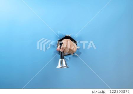 Human hand holding ringing handbell through ripped paper. Hand gestures. Mockup or Copy space. Traditional hand bell for ringing or calling attention 122593873