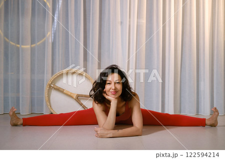 Woman in red tracksuit Sitting on a twine with a drum in a gym. Kalimeditation class 122594214