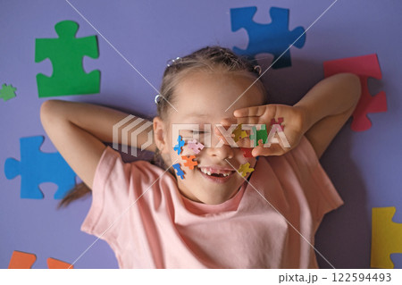Pretty Girl holds pieces of multi colored puzzles in hand, laughing and covering eyes with palm. Education and development of children of school and preschool age. Pretty Girl holds pieces of multi colored puzzles in hand, laughing and covering eyes with palm. Education and development of children of school and preschool age. 122594493