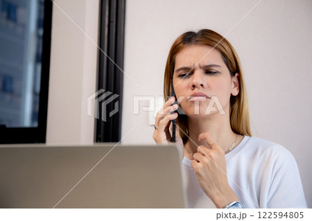 Young caucasian businesswoman working on laptop computer while talking on smartphone with stress. Young caucasian businesswoman working on laptop computer while talking on smartphone with stress. 122594805
