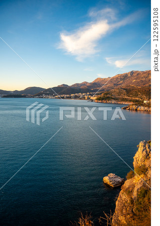 Coastal view of Becici and Budva from a rocky cliff, bathed in golden sunset light with the sea stretching toward the horizon. Coastal view of Becici and Budva from a rocky cliff, bathed in golden sunset light with the sea stretching toward the horizon. 122595108