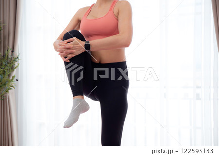 Beautiful young asian woman standing workout with warmup and stretch muscle leg at home. 122595133
