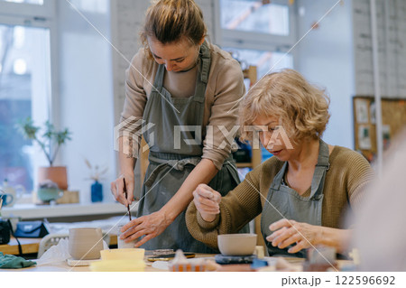 Two women work together with clay, developing skills and enjoying the artistic process. Elderly Caucasian woman learns pottery at a creative workshop with a young mentor 122596692