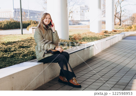 Happy 30s woman talking phone and look happy outdoors. Urban lifestyle concept. Spring time. Beautiful woman walking on the modern city street. Happy 30s woman talking phone and look happy outdoors. Urban lifestyle concept. Spring time. Beautiful woman walking on the modern city street. 122598953