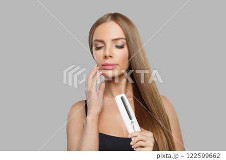Posing young female model woman with long brown smooth hairstyle holding straight iron. Posing young female model woman with long brown smooth hairstyle holding straight iron. 122599662