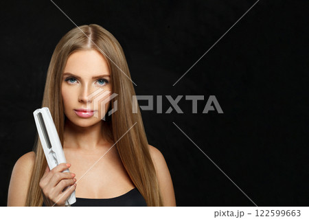 Isolated woman with hair straightener iron in studio isolated on black background. Isolated woman with hair straightener iron in studio isolated on black background. 122599663