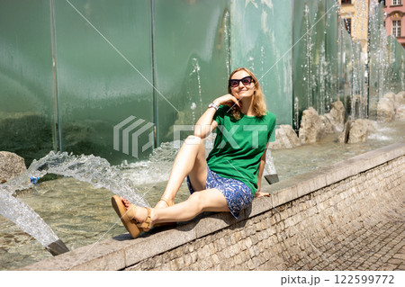 Happy 30s young female tourist is exploring new city. Woman sitting on central square in Wroclaw old town in Poland. High quality photo, summer time. Vacation concept 122599772