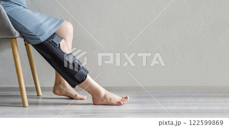 Knee brace on woman leg on grey background with copy space. Injury, medicine, arthritis and meniscus diseases concept Knee brace on woman leg on grey background with copy space. Injury, medicine, arthritis and meniscus diseases concept 122599869