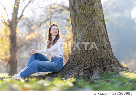 Young woman relaxing under a tree in autumn park 122599999
