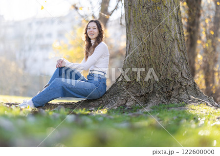Young woman relaxing under tree in autumn park 122600000