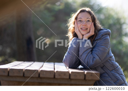 Smiling teenager with braces leaning on wooden table in park 122600010