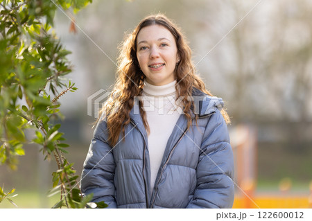 Young woman smiling outdoors, wearing braces and winter clothes 122600012