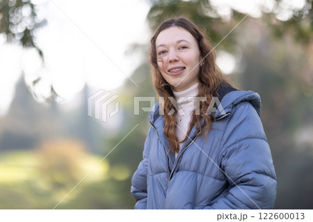 Happy student wearing dental braces is posing in a park during winter 122600013