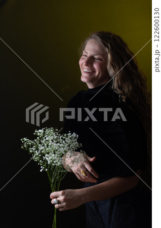 A beautiful mature woman holds a white flowers on a dark studio background. A beautiful mature woman holds a white flowers on a dark studio background. 122600130