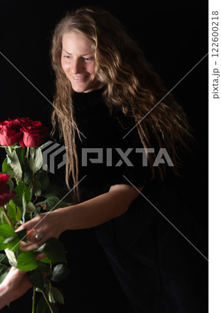 Beautiful young woman with bouquet of red roses flowers on black studio background Beautiful young woman with bouquet of red roses flowers on black studio background 122600218