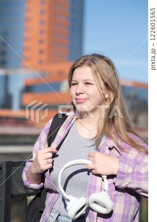 A young woman looks content while standing near a railing, the city behind her bathed in sunlight. The scene showcases the harmony of self-expression and urban exploration. A young woman looks content while standing near a railing, the city behind her bathed in sunlight. The scene showcases the harmony of self-expression and urban exploration. 122601565