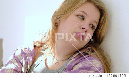A teenage girl with a distant look sits quietly, her expression reflecting contemplation. The image captures the vulnerability and complexity of human emotions. A teenage girl with a distant look sits quietly, her expression reflecting contemplation. The image captures the vulnerability and complexity of human emotions. 122601566
