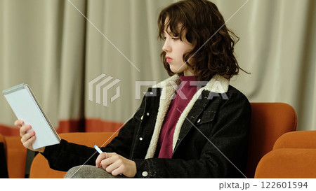 A girl playfully extends her notebook forward, her expression both focused and amusing. The photo highlights themes of creative problem-solving and lighthearted concentration. 122601594