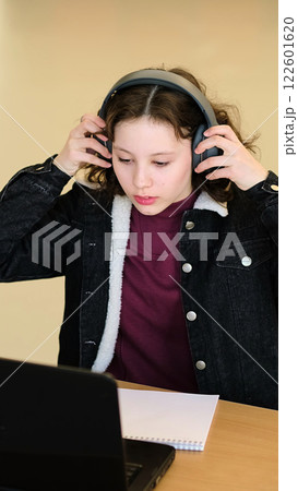 A young girl with curly hair and headphones pauses her work, offering a determined expression. This image represents youth empowerment and the importance of digital literacy in modern education. A young girl with curly hair and headphones pauses her work, offering a determined expression. This image represents youth empowerment and the importance of digital literacy in modern education. 122601620