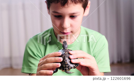A boy sits with a turtle in his hands, absorbed in observing its movements. The image emphasizes a quiet moment of discovery and compassion for small creatures. 122601696
