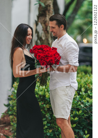 Young man gives his girlfriend a bouquet of red roses on Valentine's Day. The girl is wearing an elegant black dress. Valentine's Day Flowers Young man gives his girlfriend a bouquet of red roses on Valentine's Day. The girl is wearing an elegant black dress. Valentine's Day Flowers 122602122