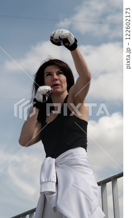 A determined woman throws a punch towards the sky, her expression filled with focus and strength. The rise of female empowerment in sports highlights resilience, confidence, and mental toughness. A determined woman throws a punch towards the sky, her expression filled with focus and strength. The rise of female empowerment in sports highlights resilience, confidence, and mental toughness. 122602173