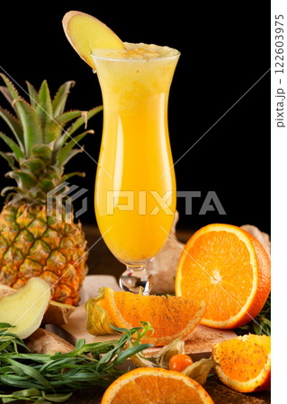 Closeup glass of fresh orange and pineapple juice decorated with ginger and fruits on a wooden table isolated at black background. Closeup glass of fresh orange and pineapple juice decorated with ginger and fruits on a wooden table isolated at black background. 122603975