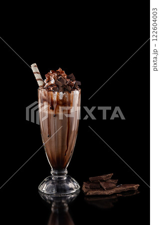 Closeup glass of chocolate milkshake decorated with caramel and whipped cream isolated at black background. 122604003
