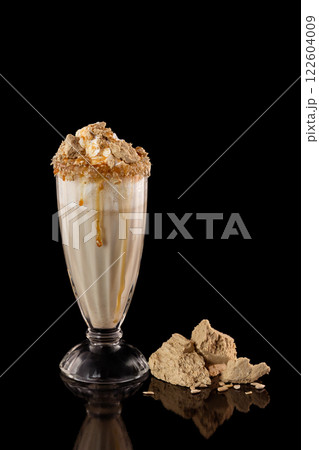 Glass of milkshake decorated with halva and caramel isolated at black background. 122604009