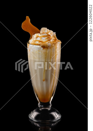 Closeup glass of caramel milkshake decorated with syrup and whipped cream isolated at black background. 122604022