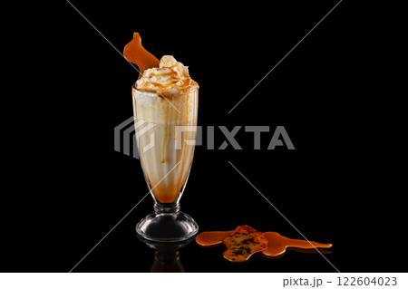 Closeup glass of caramel milkshake decorated with syrup and whipped cream isolated at black background. Closeup glass of caramel milkshake decorated with syrup and whipped cream isolated at black background. 122604023