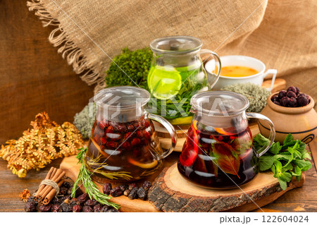 Three teapots with tea assortment decorated with nuts, citrus, black currant berries and mint at wooden table background. Three teapots with tea assortment decorated with nuts, citrus, black currant berries and mint at wooden table background. 122604024