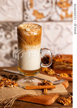 Closeup glass of latte coffee with milk foam at decorated with nuts and cinnamon wooden table background. 122604036
