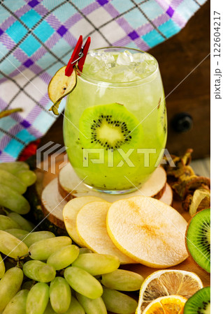 Closeup glass of healthy kiwi fresh juice with ice isolated at rural background with fresh fruits around. Closeup glass of healthy kiwi fresh juice with ice isolated at rural background with fresh fruits around. 122604217