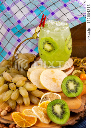 Closeup glass of healthy kiwi fresh juice with ice isolated at rural background with fresh fruits around. Closeup glass of healthy kiwi fresh juice with ice isolated at rural background with fresh fruits around. 122604218