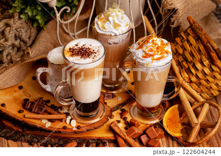 Group of three hot layered coffee glasses decorated with whipped cream foam and nuts at xmas wooden table background. 122604244