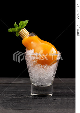 Closeup glass of cocktail with mango and pineapple juice and rum decorated with mint served in a lamp at wooden table isolated at black background. Closeup glass of cocktail with mango and pineapple juice and rum decorated with mint served in a lamp at wooden table isolated at black background. 122604257