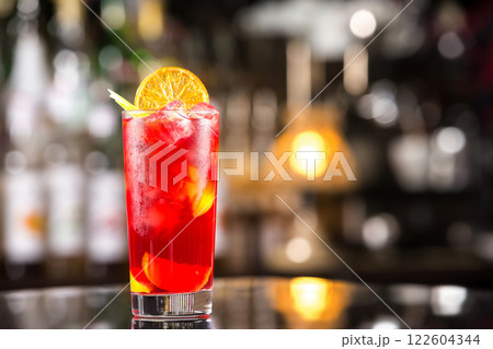 Closeup glass of cocktail with strawberry syrup, rum and lemon decorated with orange slice at bar background. Closeup glass of cocktail with strawberry syrup, rum and lemon decorated with orange slice at bar background. 122604344