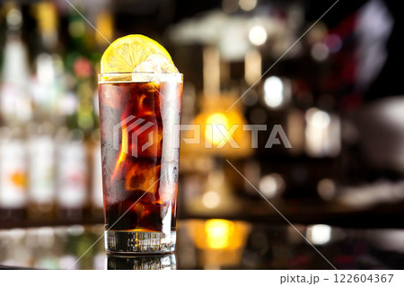 Rum cola casual cocktail with ice cubes and lemon at festive bar stand background. Rum cola casual cocktail with ice cubes and lemon at festive bar stand background. 122604367