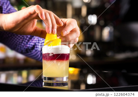 Closeup image of bartender hands decorating cocktail with lemon at dark backgrpund. 122604374