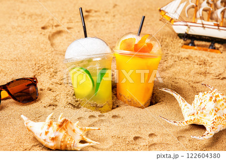 Two glasses of fresh cocktails at yellow beach sand with seashells and footprints at background. Two glasses of fresh cocktails at yellow beach sand with seashells and footprints at background. 122604380